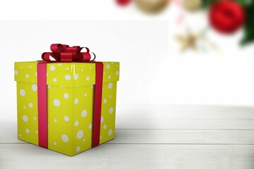 Flat-design yellow dotted gift box with red ribbon is sitting on wood table with blurred ornaments
