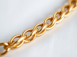 Fototapeta premium Close up of shiny gold chain with interlocking links on soft white fabric background, showcasing elegance and luxury
