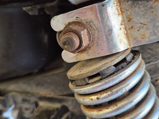 Close-up of a Rusty Bolt and Metal Bracket on a Dusty Shock Absorber Spring