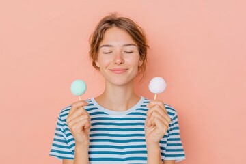 Young woman enjoying colorful ice cream pops, smiling with closed eyes, wearing striped shirt against a soft pink background, dreaming of sweet summer days and blissful moments.