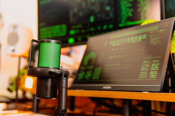A close-up of a black microphone with green LED lighting, placed in front of multiple computer...