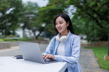Young asian woman lies outdoors in park reading book using laptop computer Education studying...