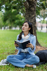 Fototapeta premium Young studying students asian woman sitting outdoors and reading a book enjoying leisure time in a park, copy space. Education studying students concept 