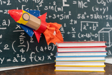 Paper rocket flying over books and chalkboard with math formulas symbolizing learning, creativity,...