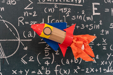 Paper rocket craft flying over chalkboard full of math formulas symbolizing creativity, learning,...