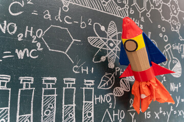 Paper rocket craft with science formulas on chalkboard background symbolizing creativity and education