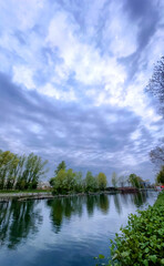 A serene river reflects lush greenery and moody clouds, making it ideal for nature and landscape themes
