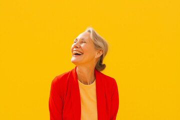 A happy senior woman laughs against a yellow background