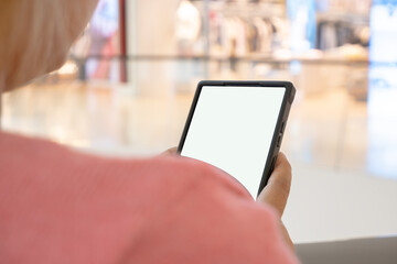 In a modern retail space, an Asian woman holds a smartphone—symbolizing digital engagement in a tech-driven shopping environment. Technology concept and white screen for your project.
