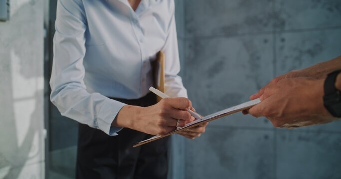 Close Up of Mailman Delivering Padded Envelope for Recipient in Modern Office. Woman Receiving Small Parcel with Online Shopping Order, Signing POD. Postal Service Worker Working in Delivery Service.