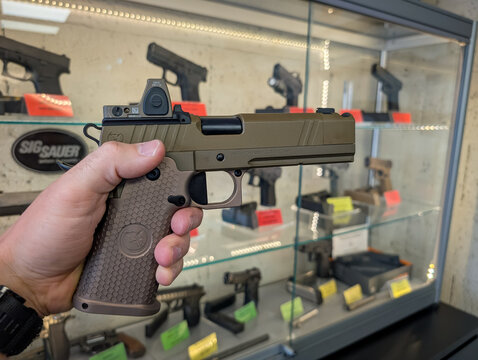 THE BALTICS &ndash; JULY 3, 2025: A man holds a Nighthawk Custom semi-automatic pistol with a Trijicon RMR red dot sight mounted on it in a gun store.