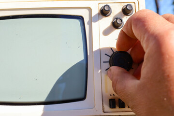 A close-up of a hand adjusting a knob on a vintage television, highlighting human interaction with...
