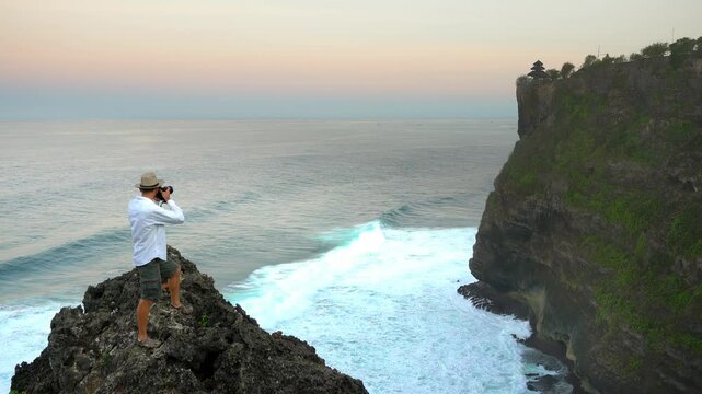Travel photographer on top mountain make photo Bali famous landmark and popular travel destination Uluwatu temple Bali, Indonesia 4K