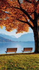 Two empty benches by lake under an autumn tree with mountains in background