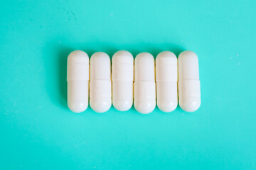 A row of white capsules is centrally arranged on a bright turquoise background. This minimalist...