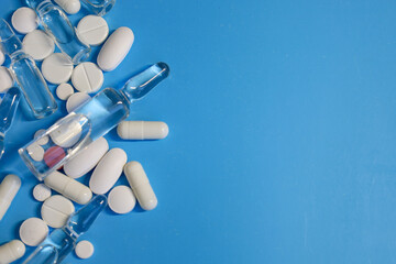 A rich blue background is adorned with a scattering of medical ampoules, white pills, and capsules, arranged in the left part of the frame. The composition symbolizes modern medicine and pharmaceutica