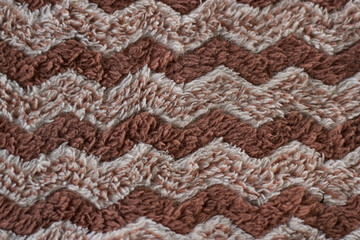 A close-up macro shot of a brown and beige shaggy rug with a chevron or zigzag pattern. A warm,...