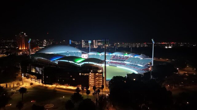 Adelaide Oval, South Australia, 2 Jul 2025: 4K Nighttime Aerial Drone Footage of the Famous Sports Stadium Illuminated in Colourful Lights, Capturing Roof Design, Seating Tiers, and Surrounding City