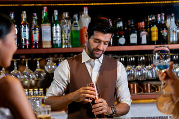 A charismatic bartender or mixologist smiles at a customer while preparing a craft cocktail with a shaker A concept for the hospitality industry and expert service