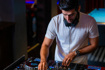 A professional DJ mixes a live set on a controller in a dark nightclub or bar A concept for...