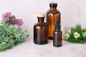 Three dark glass bottles containing essential oils arranged with vibrant herbs and blooming flowers. Natural aesthetic ideal for herbal remedies. Alternative medicine, healthy and well-being concept