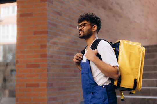 Delivery man carrying yellow thermal backpack walking near brick wall