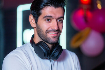 A handsome DJ focuses on his music set in a vibrant nightclub with a guest in the background A...