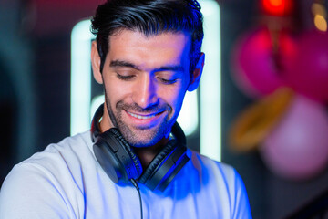 A handsome DJ focuses on his music set in a vibrant nightclub with a guest in the background A...