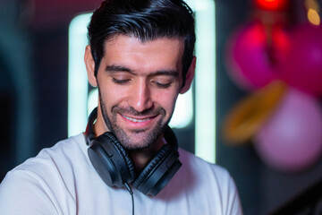 A handsome DJ focuses on his music set in a vibrant nightclub with a guest in the background A...