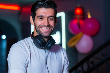 A handsome DJ focuses on his music set in a vibrant nightclub with a guest in the background A...