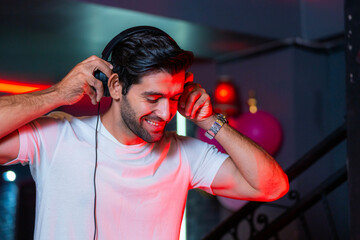A handsome DJ focuses on his music set in a vibrant nightclub with a guest in the background A...