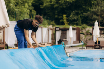 Pool maintenance worker rolling up the thermal cover of a swimming pool