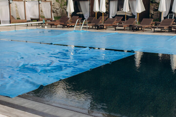 Blue pool cover being pulled across swimming pool