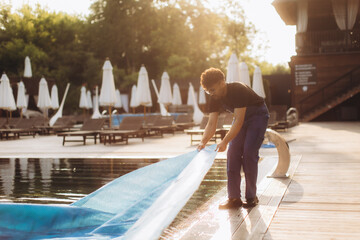 Pool maintenance worker removing solar cover at resort in the morning
