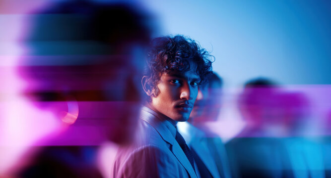 Modern male leader turning toward camera while colleagues blur past in vibrant tech-inspired setting
