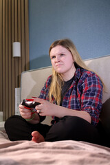 Teen girl sits barefoot on a bed with a wireless controller, showing a serious and competitive...