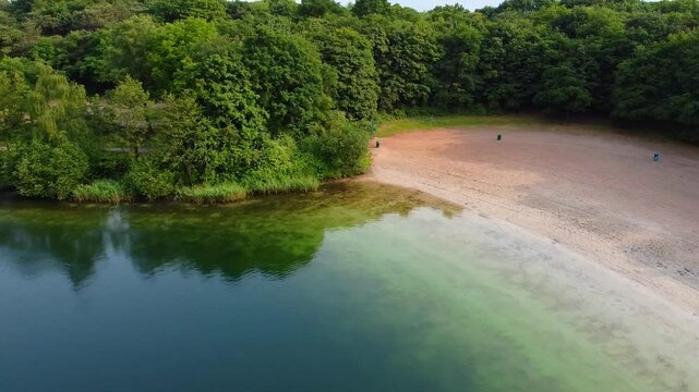 Aerial view above scenic clear water lake with peaceful empty beach with surrounding forest near Breda, Netherlands.