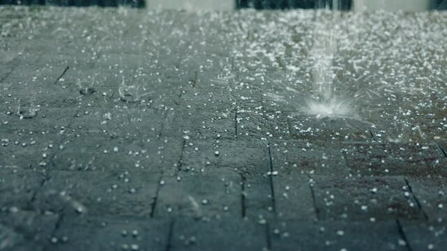 Intense hailstorm mixed with heavy rain hitting a roof covered with durable bitumen shingles, emphasizing strong weather impact and roofing protection.