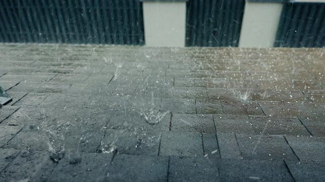 Heavy rain with hailstorm falling on a roof covered with durable bitumen shingles, highlighting strong weather and reliable roofing materials.