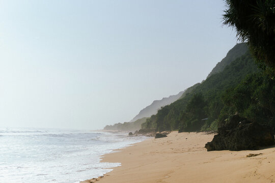 Untouched tropical beach with waves and lush green cliffs