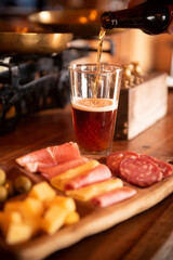 Beer served on a glass next to cold meat, cheese and ham