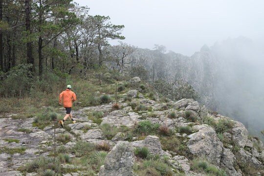 One man running on a rocky trail at high mountain during a foggy day.
