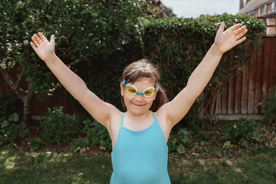Smiling child girl in swimsuit raising her arms with in a garden.