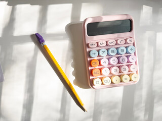Pastel calculator and pencil on white desk in sunlight