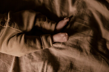 Baby in waffle knit pajamas lying on soft beige bedding.