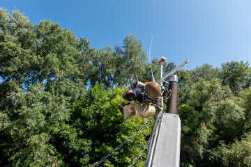 Detail of old boat horn, loudspeaker and antennas with chains on a mast, against blue sky and green trees during a sunny day on the Bodrog river.