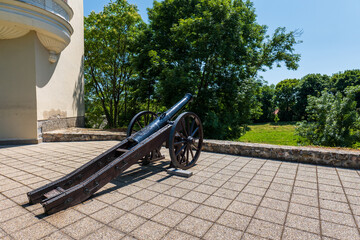 Old black cannon on wooden wheels placed on a stone terrace near Sárospatak Castle, Hungary, with green trees in the background on a sunny day.