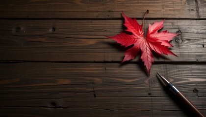 A vibrant red maple leaf and pen resting on rustic dark wooden planks creating an autumnal scene