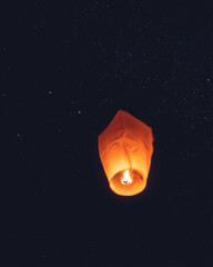 Glowing orange sky lantern floating against a dark, starry night sky, symbolizing hope and celebration.