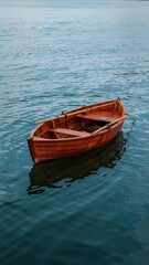 Fototapeta premium Minimalist Aerial View of Red Wooden Rowboat Floating in Calm Deep Blue Water with Gentle Ripples